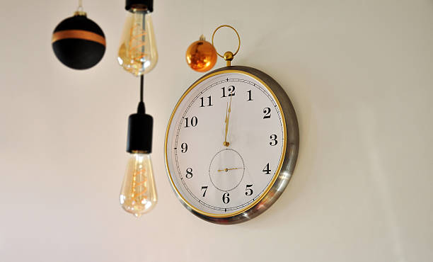 istock Clock strikes twelve, minute after midnight. Round clock on a light wall, midnight time, New Year's Eve concept 2253633065