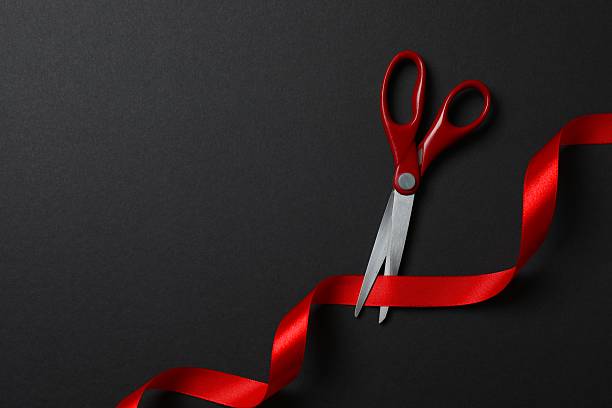 istock Scissors cutting red ribbon isolated on black surface 2253633478