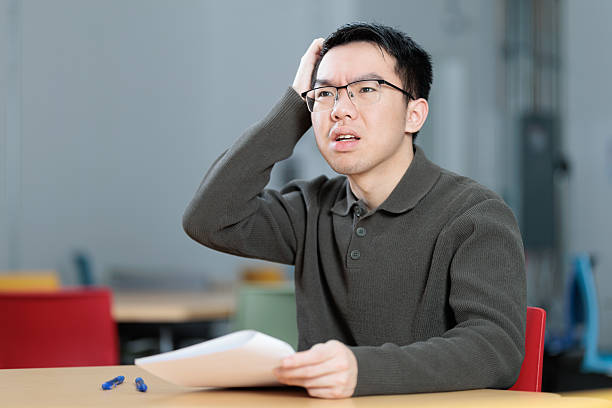 istock Confused student scratching head while studying at desk in classroom 2253637339