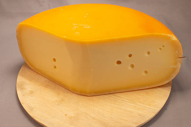 Gouda Cheese Wheel On Wooden Board Glossy Rind Smooth Pale Interior, StudioLit Display For Cheesemonger Sampling And Retail Presentation,