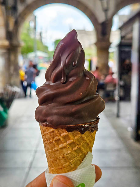 istock Chocolate-dipped soft-serve ice cream cone held in a vibrant outdoor setting 2253639342