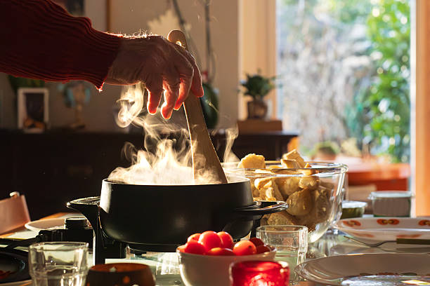 Cozy dining scene featuring a steaming cheese fondue surrounded by bread and glasses. The hand in the frame suggests sharing food and spending time together. Ideal for winter coziness, holidays and social moments at home.