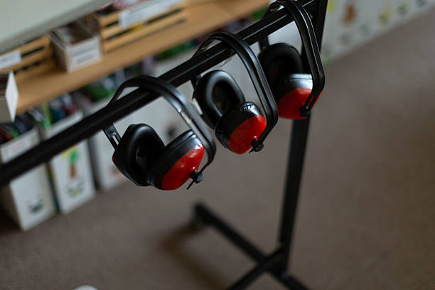 red safety earmuffs hanging on rack, blurred classroom shelf with labeled bins, soft daylight, tidy setup for noisy craft