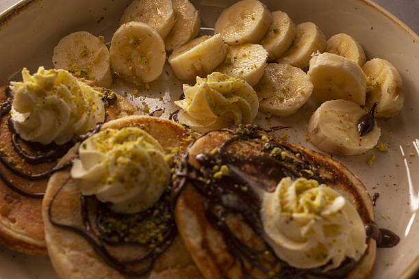 banana cream pancakes stacked with sliced banana and whipped cream, syrup drizzle, cinnamon dust, brunch chef plating, warm morning light, comfort cafe breakfast moment, instagrammable shot