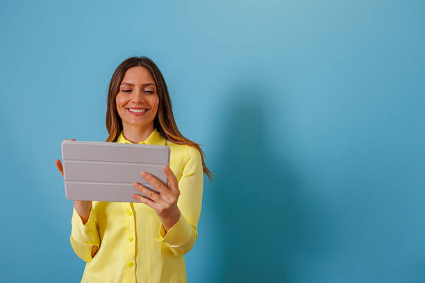 istock Smiling woman holding a tablet for communication and entertainment. She is using technology for online content on a blue background 2253645400