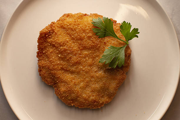 Golden browned breaded meat, Fried cutlet with fresh parsley garnish, Highresolution image showcasing golden fried breaded cutlet with parsley on white plate