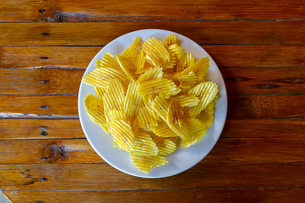 Chifles. A traditional South American snack of crunchy fried plantain chips. Carefully arranged on a white plate. Resting on a rustic wooden table. Offering a delicious and authentic taste experience