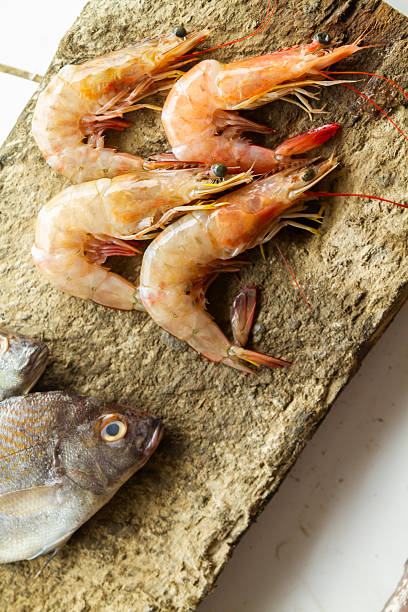 Grouping of sea fresh raw shrimp and a golden fish presented on a rustic stone cutting board, emphasizing healthy eating, seafood preparation, and traditional South American cuisine