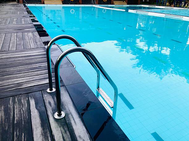 swimming pool with stainless steel ladder and wooden deck under bright daylight