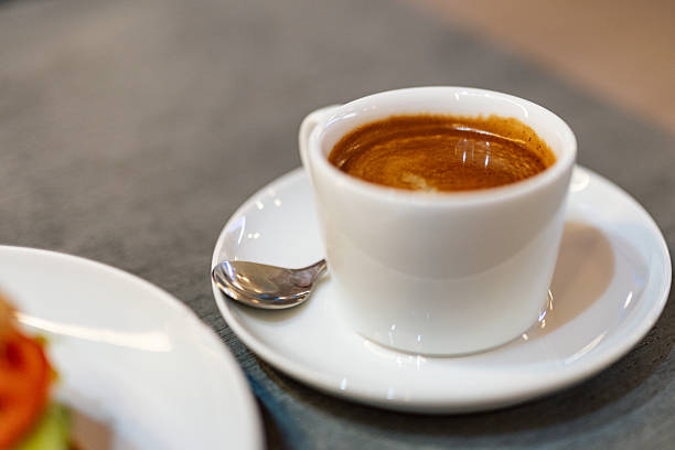 Espresso coffee served in a white ceramic cup on a saucer with a spoon, photographed indoors with shallow depth of field and copy space.