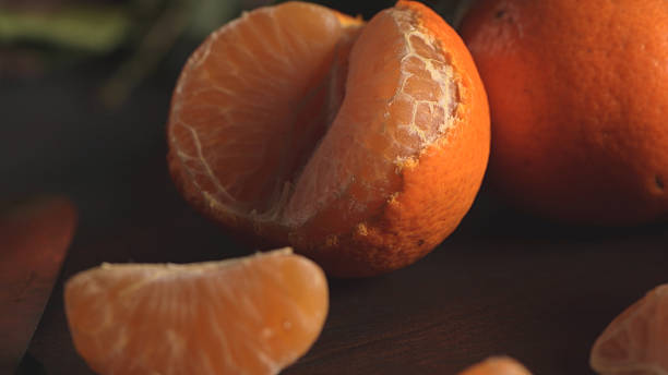 istock Partially peeled mandarin orange and segments on a dark wood surface 2253651506