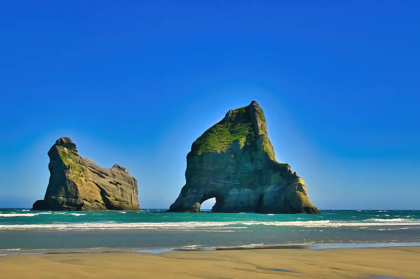 One of the Archway Islands off the coast of Wharariki Beach, Cape Farewell, South Island, New Zealand. Beach with beach pools in foreground