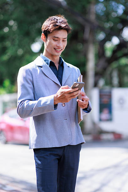 istock Young asian businessman smiling using phone outdoors 2253655161