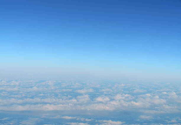 Stunning aerial view above white fluffy clouds under a clear blue sky. Bright horizon line captured from an airplane window. Peaceful and calm atmosphere for travel and nature background concepts.