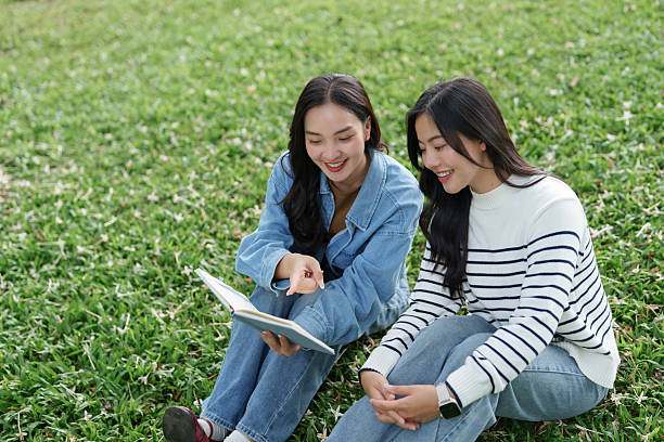 Two cheerful friends learning and discussing content while sitting on green grass