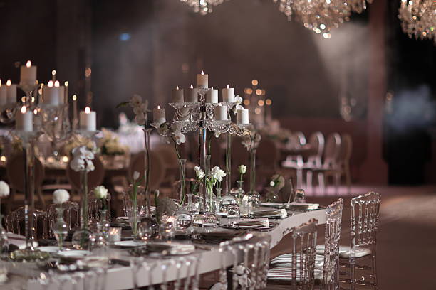 Elegant wedding reception setup featuring crystal candle holders, soft white floral arrangements, and refined table settings. Warm ambient lighting and a sophisticated atmosphere create a romantic and upscale event scene. Ideal for concepts such as luxury weddings, fine dining, celebration, elegance, romance, and premium event design. stock photo