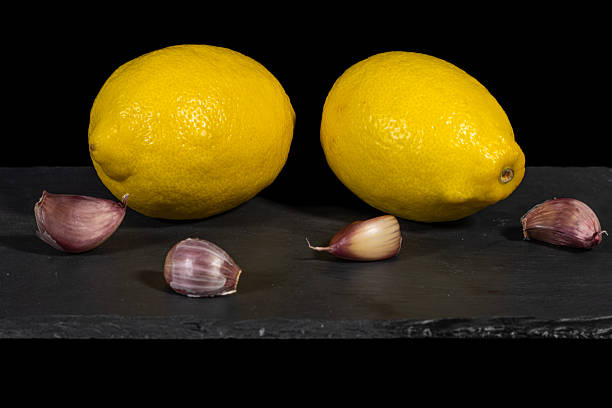 Vibrant yellow lemons and purple garlic cloves carefully displayed on a textured dark slate surface against a solid black backdrop, highlighting fresh, healthy ingredients for cooking and food projects.