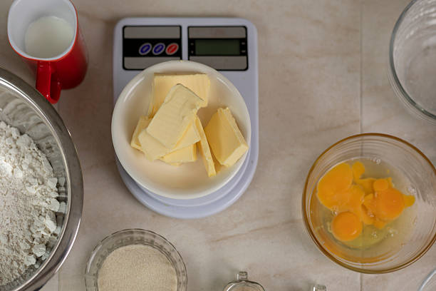 Kitchen table with baking ingredients. Sliced butter on a digital scale, flour in a bowl, cracked eggs, yeast, milk