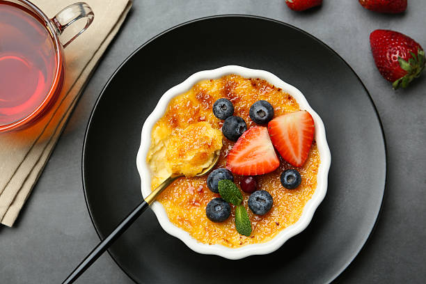 istock Delicious creme brulee with berries and mint in bowl served on grey table, flat lay 2253661513