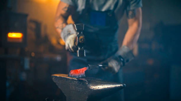 istock Focused Young Artisan Hammering Glowing Steel in Craft Workshop 2253662873