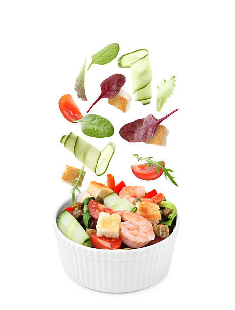 istock Ingredients falling into bowl with tasty salad on white background 2253664484