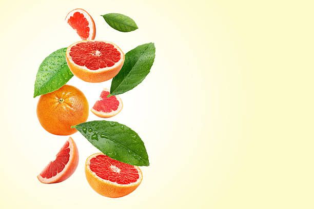 istock Fresh grapefruits and green leaves falling on light yellow background. Space for text 2253664734