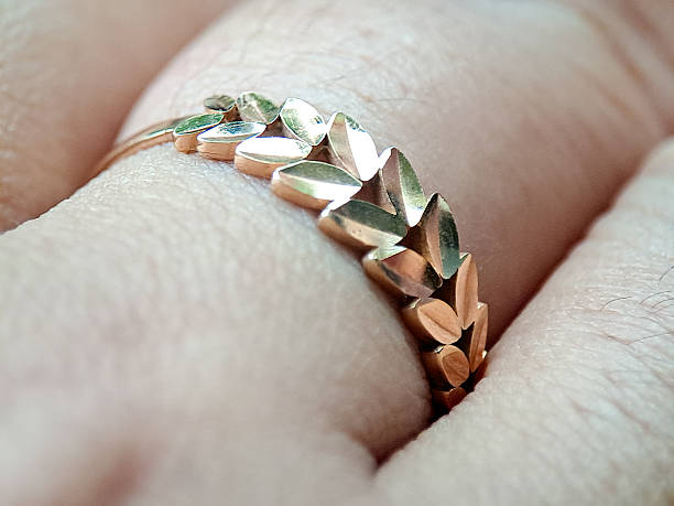 gold ring worn on a finger, featuring leaf-shaped links, photographed indoors in soft natural light, highlighting fine jewelry, elegance, texture, and minimalist fashion style.