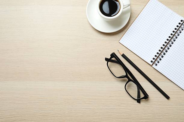 istock Office table with notebook, pencil, coffee cup and glasses, top view 2253667135