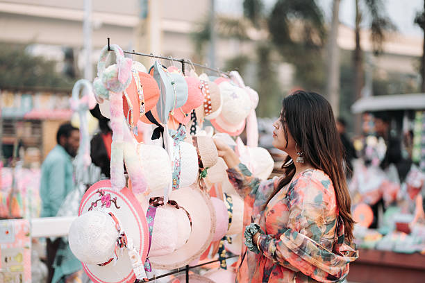 Casual female shopper browsing a variety of decorative hats at an outdoor stall. Urban lifestyle, leisure shopping, and local market culture.
