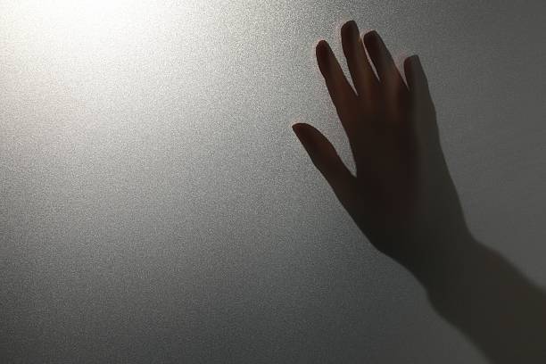 Silhouette of ghost behind glass against light grey background, closeup. Space for text