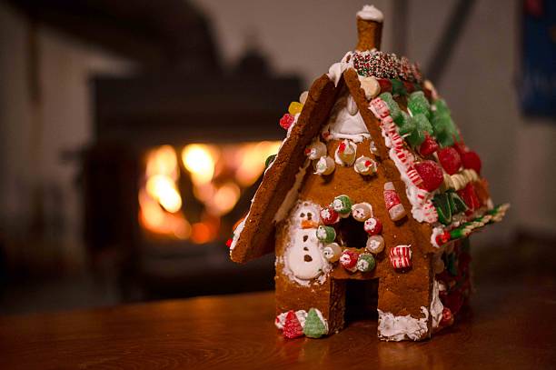 Bokeh firepace background with copy space and no people. Homemade child's gingerbread house in foreground with candy and icing warm welcoming holiday scene
