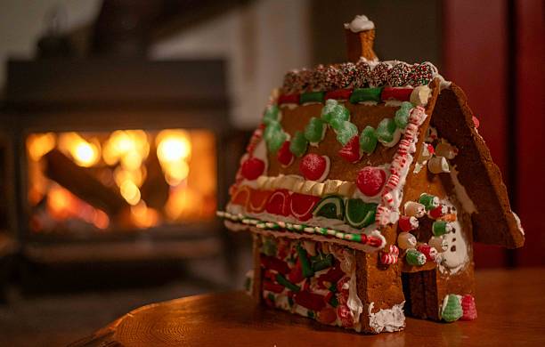 Bokeh firepace background with copy space and no people. Homemade child's gingerbread house in foreground with candy and icing warm welcoming holiday scene