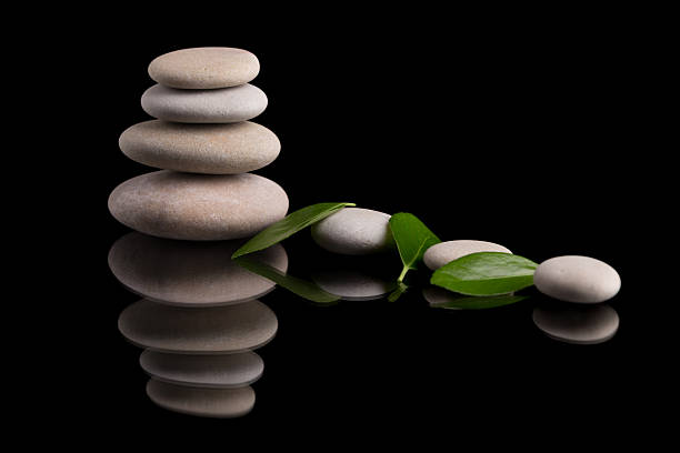 A balanced stack of smooth gray stones with fresh green leaves. This image evokes a zen-like sense of peace, balance, and nature against a black background.