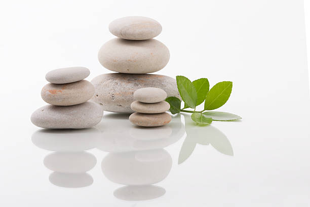 Arrangement of balanced stone stacks with green leaves on a white surface, creating a zen-like and harmonious composition. Great for concepts of balance, wellness, and relaxation.