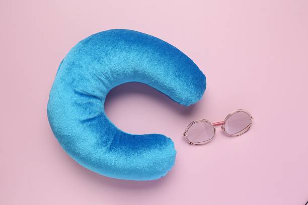 Light blue travel pillow and sunglasses on pink background, flat lay