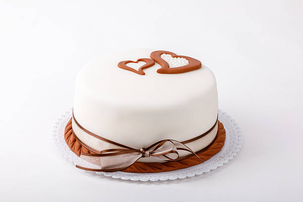 Isolated minimalist round cake with white frosting, brown ribbon, brown rope decoration, and two brown hearts on top. Great for wedding and romantic concepts.