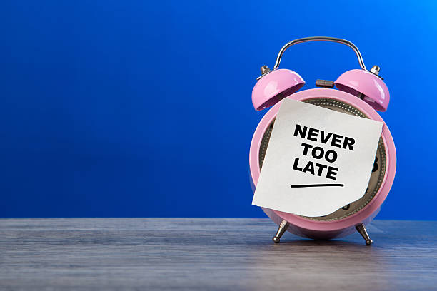 istock Pink alarm clock holding never too late sticky note 2253670907
