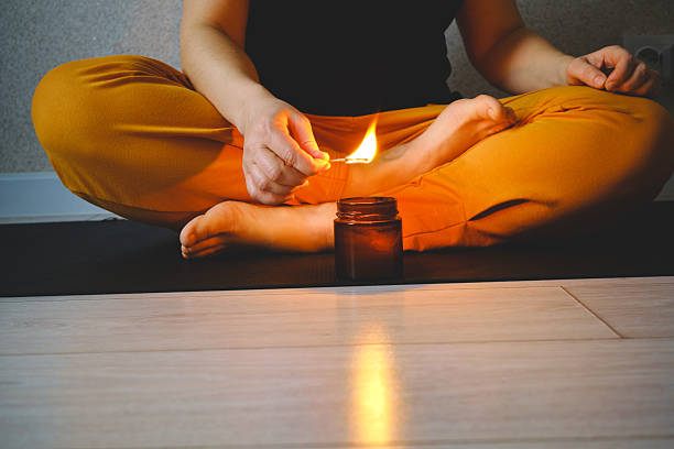 istock Person sitting in yoga pose on mat, lighting match for aromatherapy 2253686820