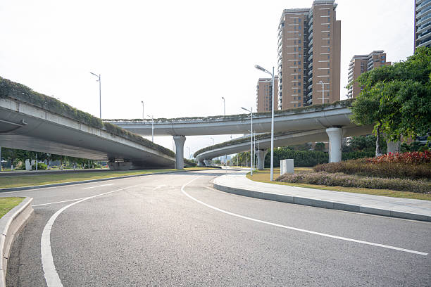 A wide urban road leading towards an elevated highway overpass, surrounded by high-rise buildings and greenery. The scene is calm and well-maintained, suitable for transportation or urban planning concepts.