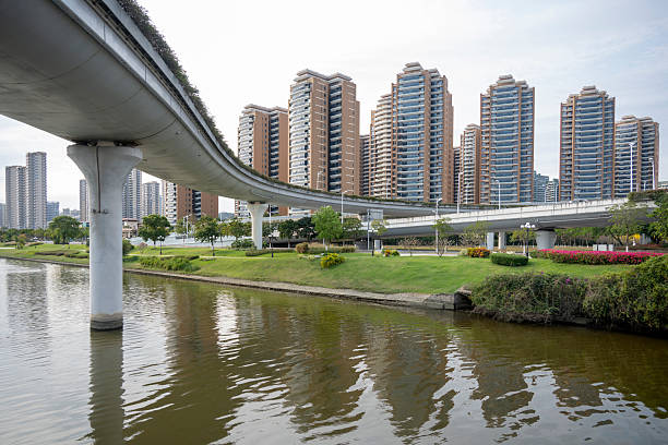 A serene cityscape featuring modern high-rise buildings alongside a tranquil river, lush greenery, and vibrant flowers. The visual style is contemporary, capturing a peaceful urban environment. Potential usage includes real estate promotion, travel brochures, or architectural showcases.