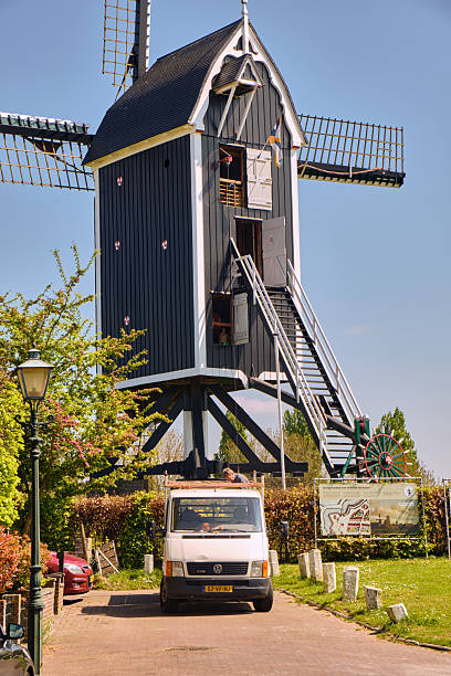 A rebuilt post mill windmill stands tall in Den Briel Netherlands with a van parked nearby. This image showcases traditional Dutch architecture and the rural landscape of a popular European travel destination.