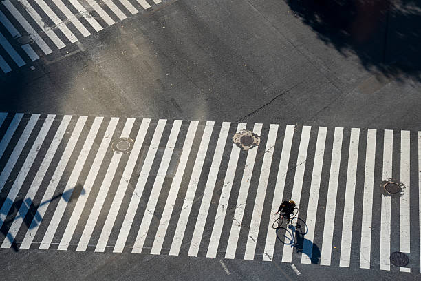 istock A high-angle shot captures a lone cyclist with a green backpack navigating a striking graphic pedestrian crossing. 2253698579