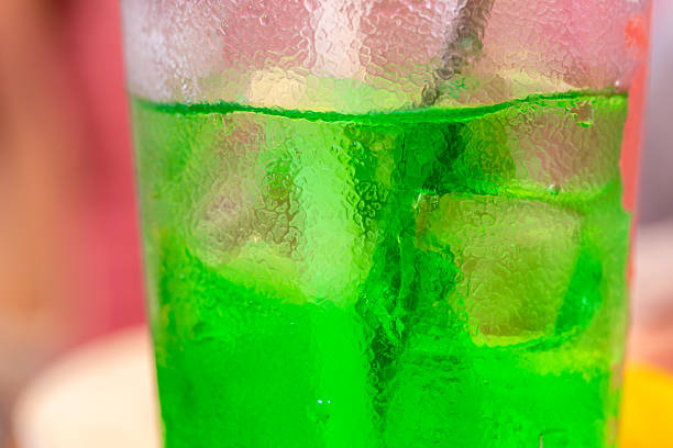 A child is drinking a refreshing, bright green, fizzy drink filled with ice, against a backdrop of bright pink.