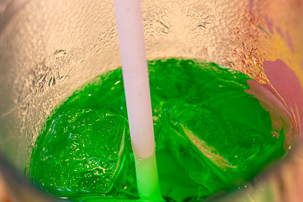 A child is drinking a refreshing, bright green, fizzy drink filled with ice, against a backdrop of bright pink.