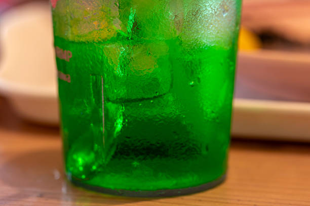 A child is drinking a refreshing, bright green, fizzy drink filled with ice, against a backdrop of bright pink.