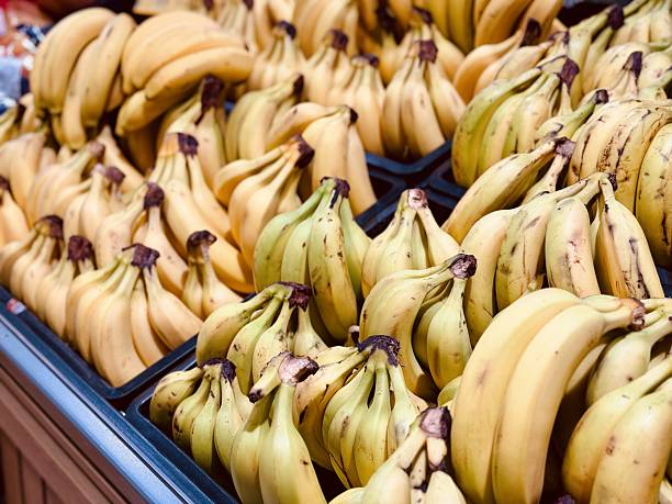 Ripe Yellow Bananas Piled In Bunches, CloseUp Market Display With Vendor Stall Ambiance, Bright Natural Light Highlighting Textured Peels And Small Brown Spots, FarmToTable Freshness