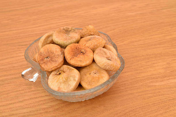 Dried figs in apple-shaped glass bowl on the wooden table. Close-up. Copy space. Selective focus.