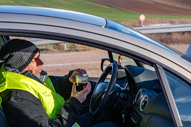 Driver in the foreground placing a V16 warning or emergency beacon with a broken-down vehicle on the road, pre-signaling. Beacon mandatory in Spain by 2026. Tordesillas, Valladolid, Castile and León, Spain, Europe - December 21, 2025.