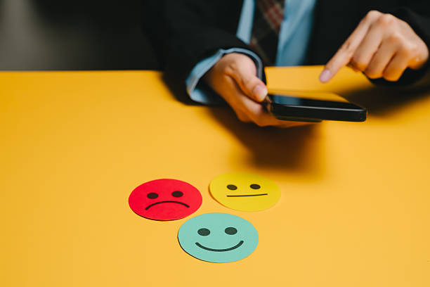 istock Feedback concept. Customer feedback concept with colorful emoticon faces and person holding smartphone on yellow table 2253731704