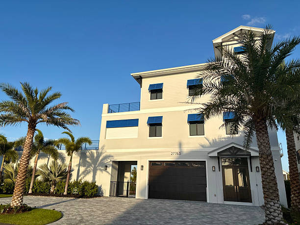Bonita Springs, Florida, United States of America - December 23, 2025: New modern home with blue hurricane shutters and palm trees standing tall, representing resilience and real estate development in Bonita Springs, Florida